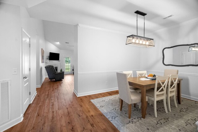 dining area featuring vaulted ceiling, crown molding, a chandelier, and wood-type flooring