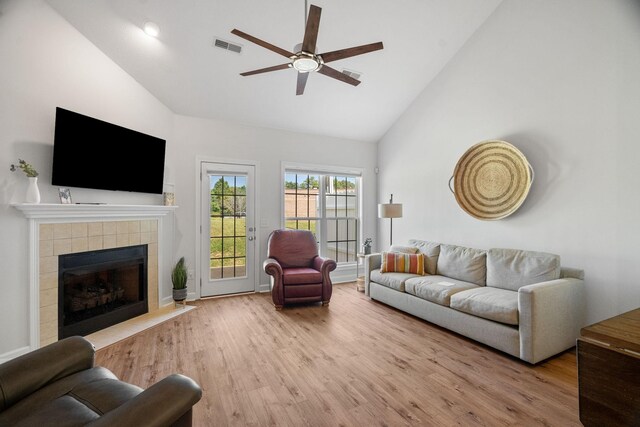 living room with ceiling fan, high vaulted ceiling, light hardwood / wood-style floors, and a tile fireplace