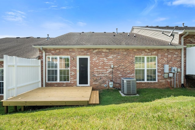 rear view of house featuring roof with shingles, a lawn, brick siding, and central AC unit