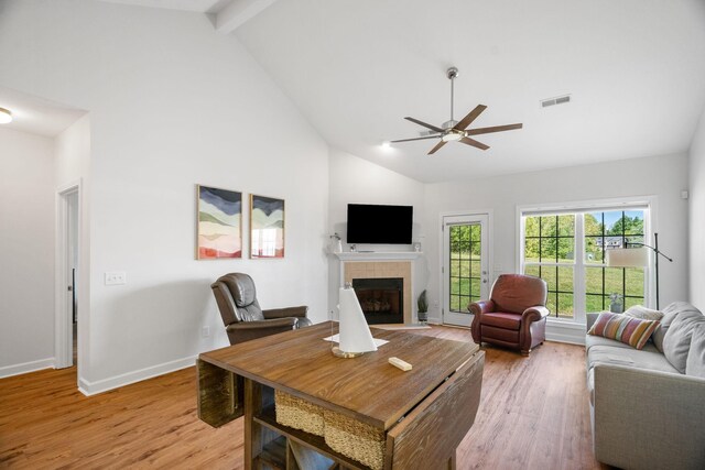 living room with high vaulted ceiling, beamed ceiling, light hardwood / wood-style floors, and a tile fireplace