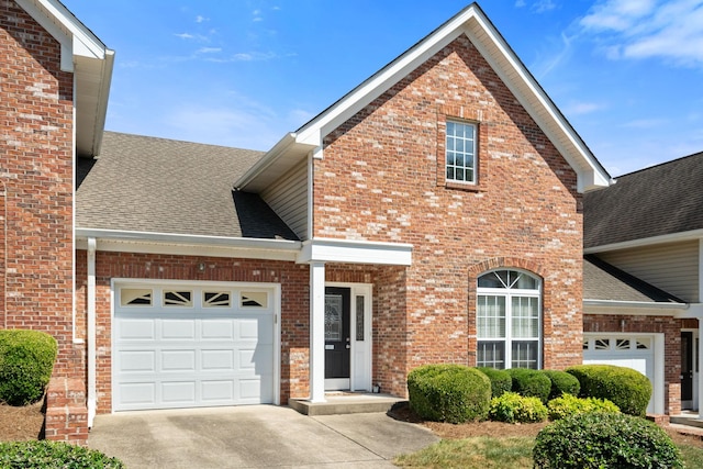 traditional home featuring a garage, concrete driveway, roof with shingles, and brick siding