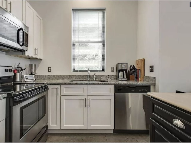 kitchen with tile patterned floors, white cabinetry, sink, dark stone countertops, and stainless steel appliances