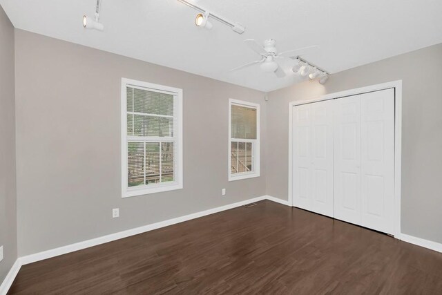 unfurnished bedroom featuring ceiling fan, rail lighting, and dark wood-type flooring