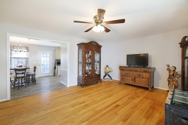 living room with ceiling fan with notable chandelier and light hardwood / wood-style floors