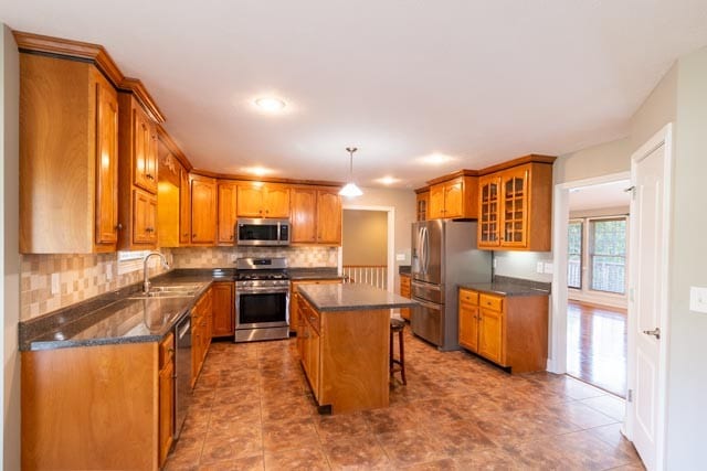 kitchen with a center island, sink, appliances with stainless steel finishes, decorative light fixtures, and a kitchen bar