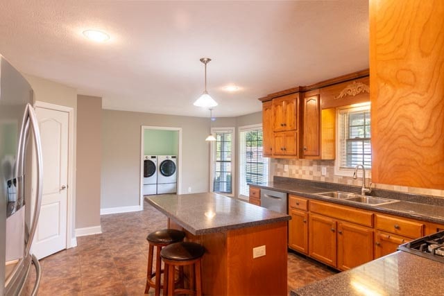 kitchen with washing machine and clothes dryer, sink, a center island, pendant lighting, and appliances with stainless steel finishes