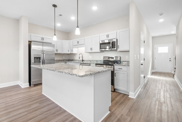 kitchen featuring recessed lighting, appliances with stainless steel finishes, a kitchen island, light stone countertops, and light wood-type flooring