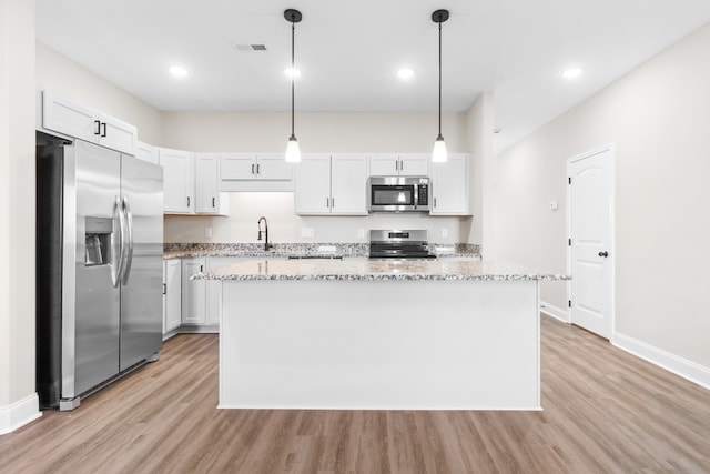 kitchen with stainless steel appliances, a center island, visible vents, light wood-type flooring, and light stone countertops