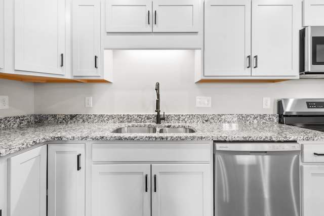 kitchen with light stone counters, white cabinetry, stainless steel appliances, and a sink