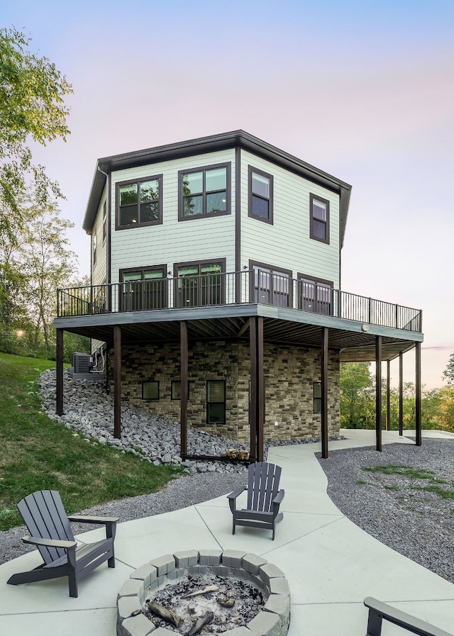 back house at dusk with an outdoor fire pit, a deck, a patio area, and central air condition unit