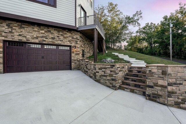 property exterior at dusk featuring a balcony and a garage