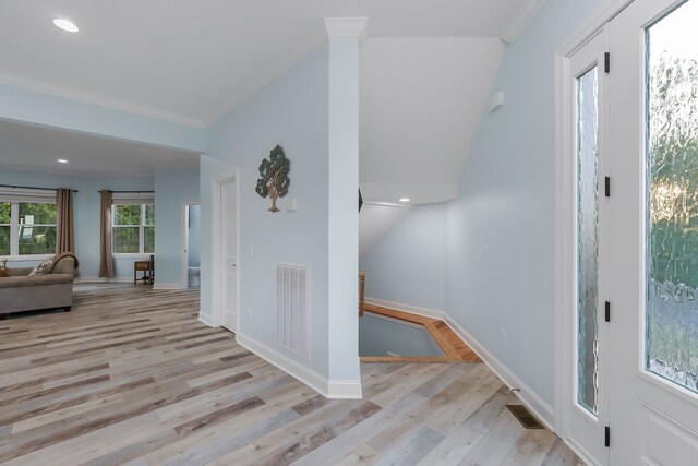 entryway with light wood-type flooring, ornamental molding, and lofted ceiling