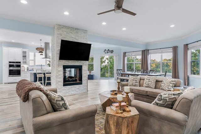 living room with ceiling fan, light hardwood / wood-style flooring, ornamental molding, and a fireplace