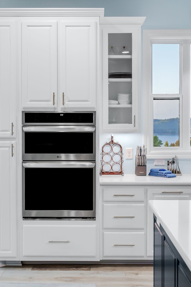 kitchen with stainless steel double oven, white cabinets, and light wood-type flooring