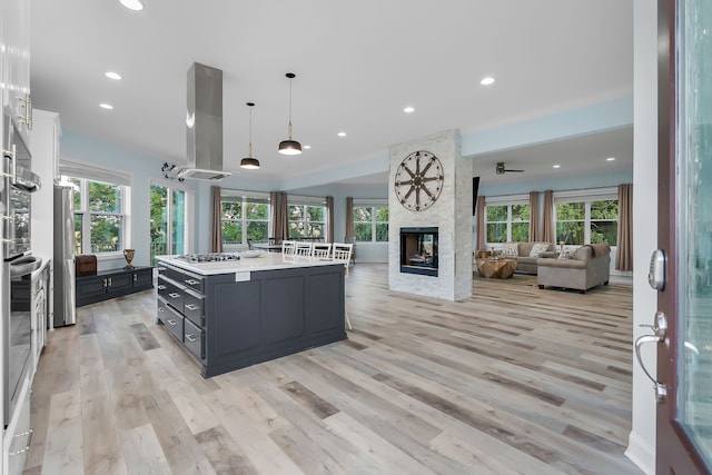 kitchen with light hardwood / wood-style flooring, island range hood, a multi sided fireplace, plenty of natural light, and a center island