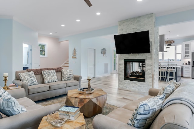 living room with ornamental molding, light hardwood / wood-style floors, and a stone fireplace