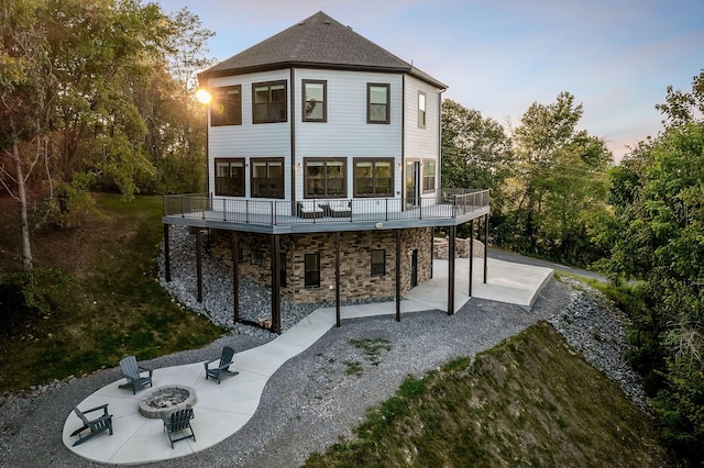 back of house at dusk with an outdoor fire pit, stone siding, a patio, and a wooden deck