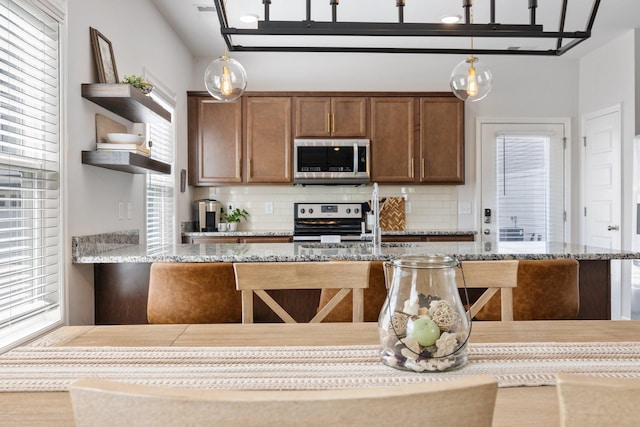 kitchen with backsplash, hanging light fixtures, stainless steel appliances, and a healthy amount of sunlight