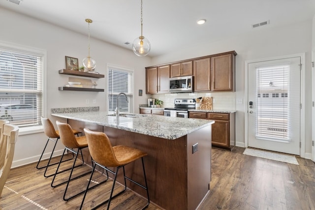 kitchen with appliances with stainless steel finishes, hanging light fixtures, light stone countertops, sink, and kitchen peninsula