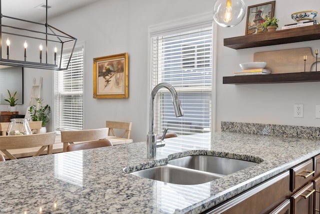 kitchen featuring sink, a notable chandelier, hanging light fixtures, and light stone counters