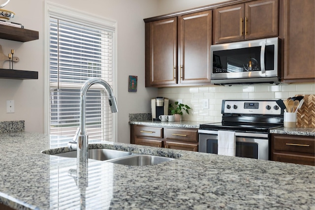 kitchen featuring decorative backsplash, stainless steel appliances, light stone countertops, and sink