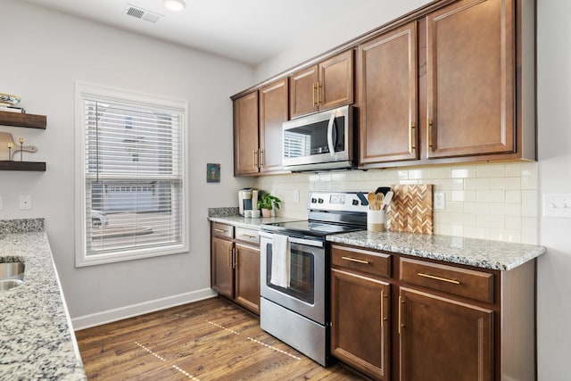 kitchen featuring appliances with stainless steel finishes, light stone countertops, backsplash, and dark hardwood / wood-style flooring