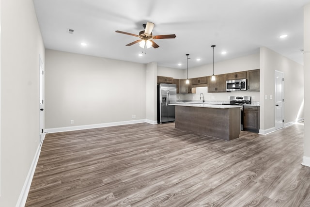 kitchen featuring stainless steel appliances, a ceiling fan, open floor plan, dark brown cabinets, and wood finished floors