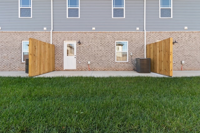 back of house featuring central AC unit, a lawn, and brick siding