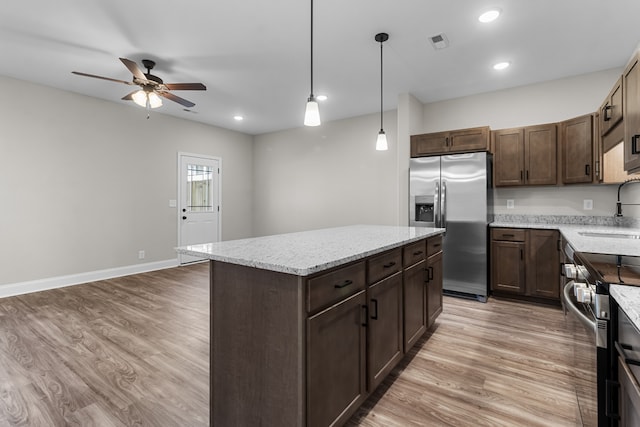 kitchen with stainless steel appliances, a sink, light wood-style floors, dark brown cabinets, and a center island