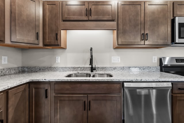 kitchen with dark brown cabinetry, appliances with stainless steel finishes, light stone counters, and a sink