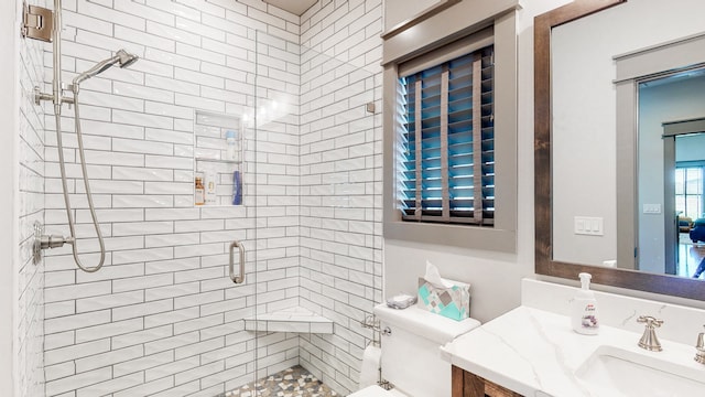 bathroom with toilet, tiled shower, and vanity