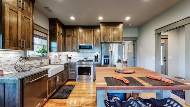 kitchen with tasteful backsplash, appliances with stainless steel finishes, light stone countertops, light hardwood / wood-style floors, and sink