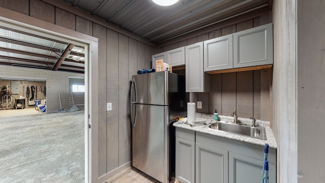 kitchen featuring wood walls, sink, gray cabinetry, stainless steel fridge, and light carpet