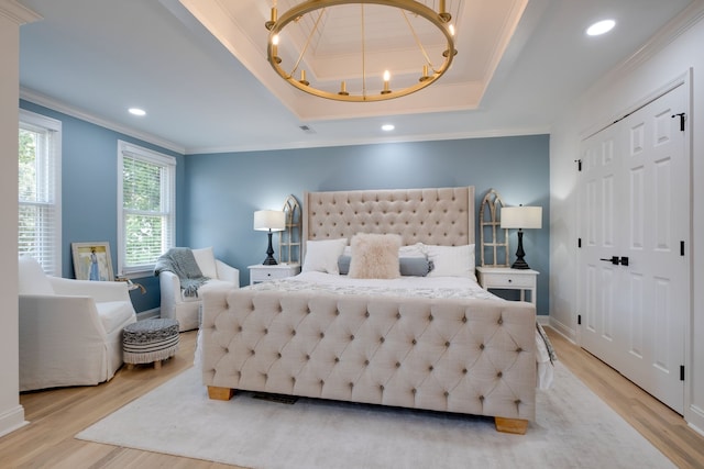 bedroom featuring light hardwood / wood-style floors, a raised ceiling, an inviting chandelier, and crown molding