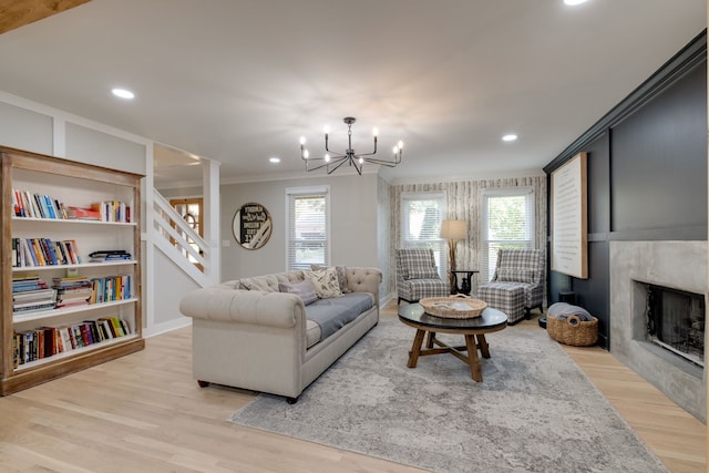 living room with built in shelves, light wood-type flooring, a fireplace, a chandelier, and crown molding