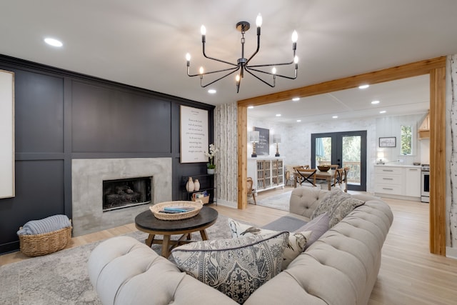 living room with a notable chandelier, light hardwood / wood-style floors, a high end fireplace, and french doors