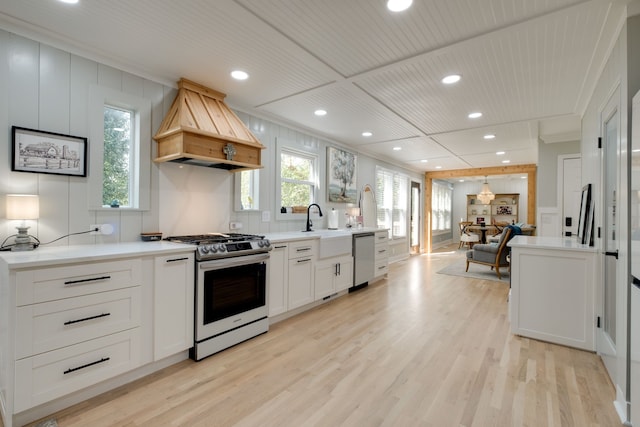 kitchen with light wood-type flooring, appliances with stainless steel finishes, sink, and premium range hood