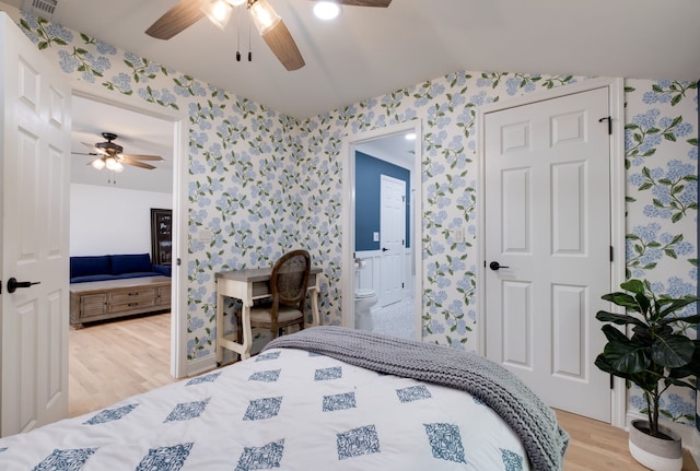 bedroom featuring ceiling fan, ensuite bath, light hardwood / wood-style flooring, and lofted ceiling