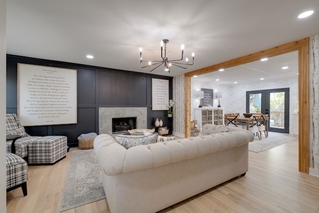 living room featuring a notable chandelier, light hardwood / wood-style flooring, french doors, and a fireplace