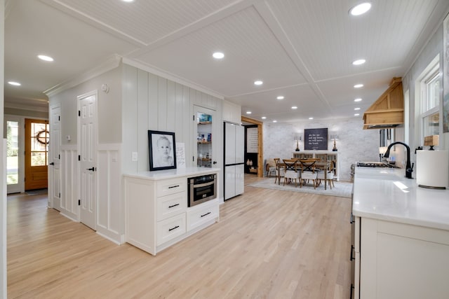 kitchen featuring sink, ornamental molding, light hardwood / wood-style floors, coffered ceiling, and white cabinetry