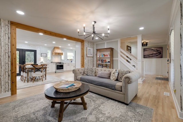 living room featuring built in features, light wood-type flooring, an inviting chandelier, and french doors