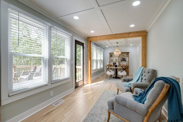 living area featuring beam ceiling, crown molding, light hardwood / wood-style flooring, and a healthy amount of sunlight