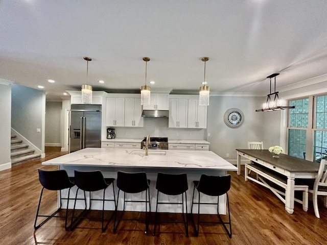 kitchen with light stone counters, a kitchen island with sink, dark hardwood / wood-style floors, stainless steel appliances, and white cabinets