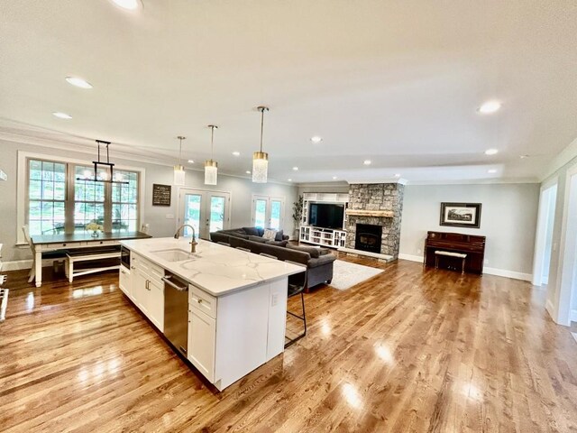 kitchen featuring light wood-type flooring, stainless steel dishwasher, a stone fireplace, white cabinets, and sink