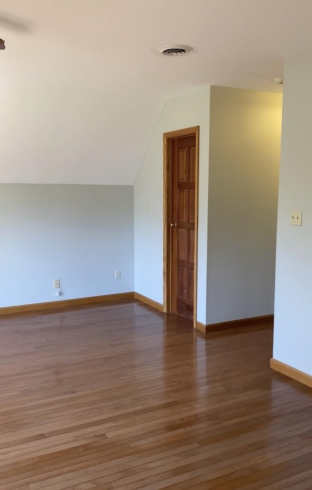 spare room with vaulted ceiling, wood finished floors, visible vents, and baseboards