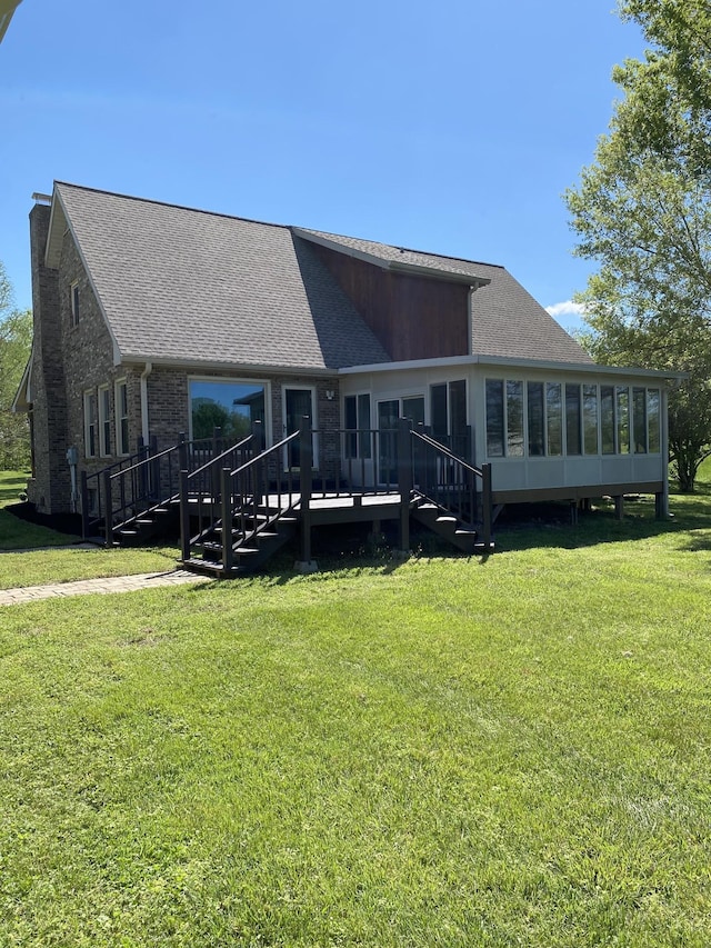 rear view of house featuring a yard, roof with shingles, a wooden deck, and a sunroom