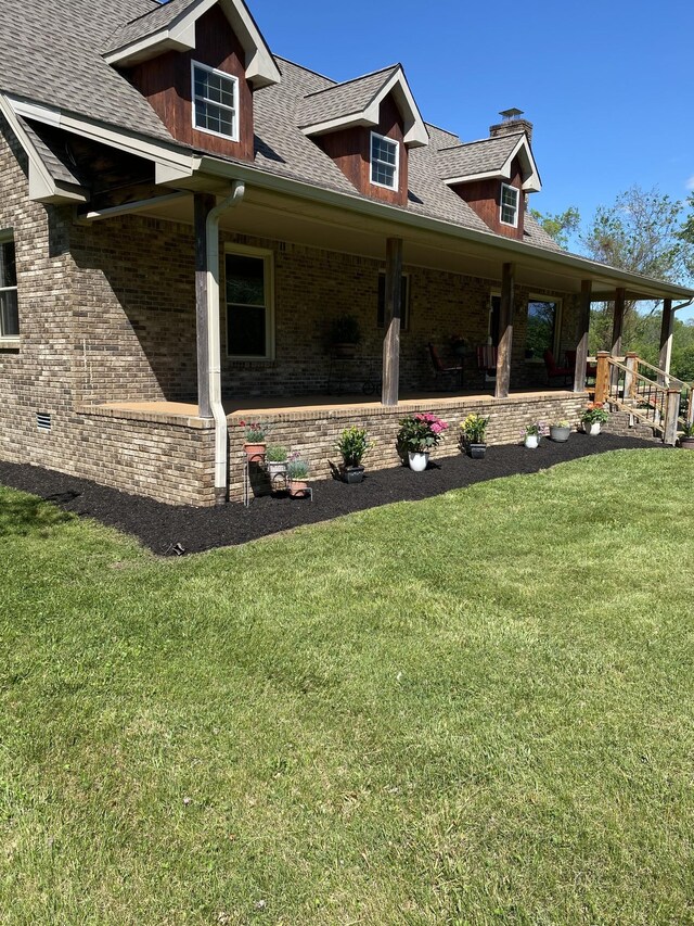 view of property exterior with brick siding, a patio area, a yard, and roof with shingles