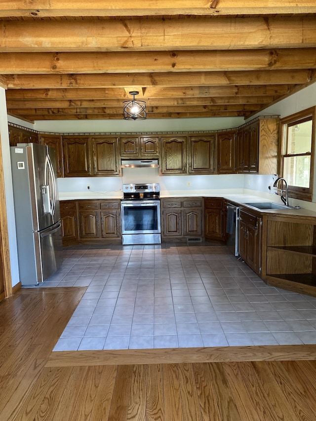 kitchen with beamed ceiling, appliances with stainless steel finishes, sink, and light hardwood / wood-style floors