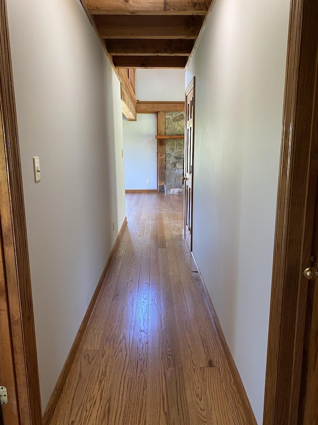 corridor with beam ceiling, baseboards, and wood finished floors