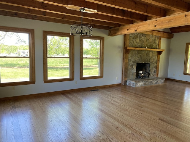 unfurnished living room featuring a stone fireplace, beamed ceiling, baseboards, and wood finished floors